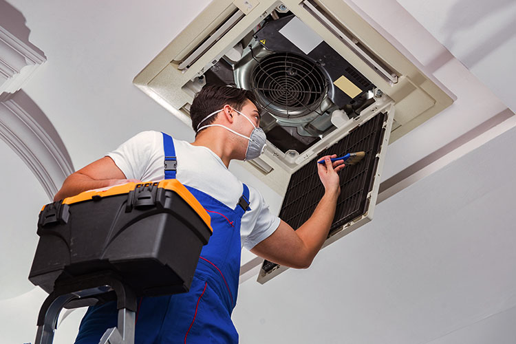 Technician repairing ceiling air conditioning unit.